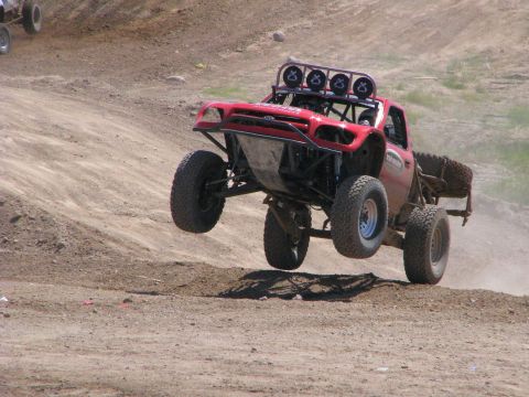2008 Ford Bronco - A red off-road truck jumps over a dirt track, with another vehicle visible in the background.