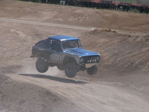 2008 Ford Bronco - A blue off-road truck with racing number 1470 soars through the air during a race on a dirt track.