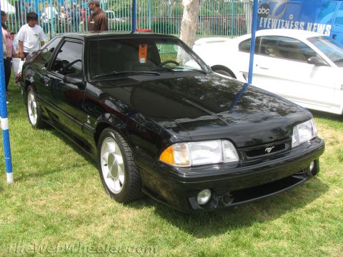 1968 Ford Mustang - This black Ford Mustang is parked on grass, with a white car and a news van in the background.