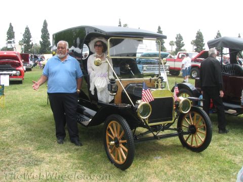 1968 Ford Mustang - A man gestures towards a vintage car with American flags on the front, while a woman in period attire sits inside.