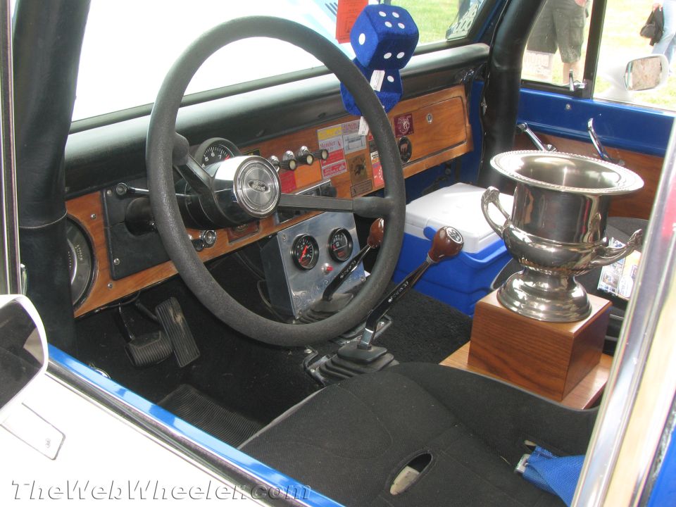 Interior shot of a vehicle, showing steering wheel, dashboard with gauges, gear shifter, and a trophy on the passenger seat
