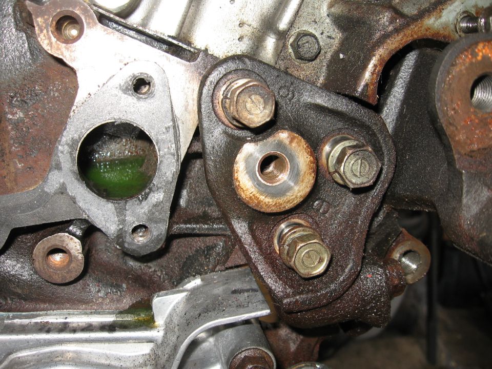 Rusty engine bracket bolted to aluminum block beside coolant port with green residue
