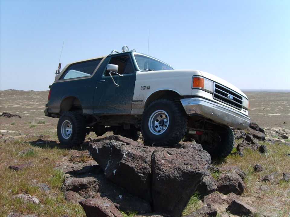 White and green lifted Ford Bronco on rocks in desert, front-three-quarter view