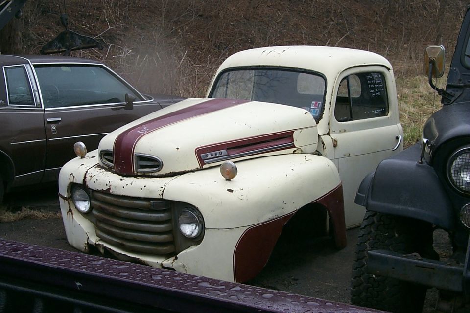 Vintage cream and maroon Ford F-Series pickup with patina parked in a junkyard