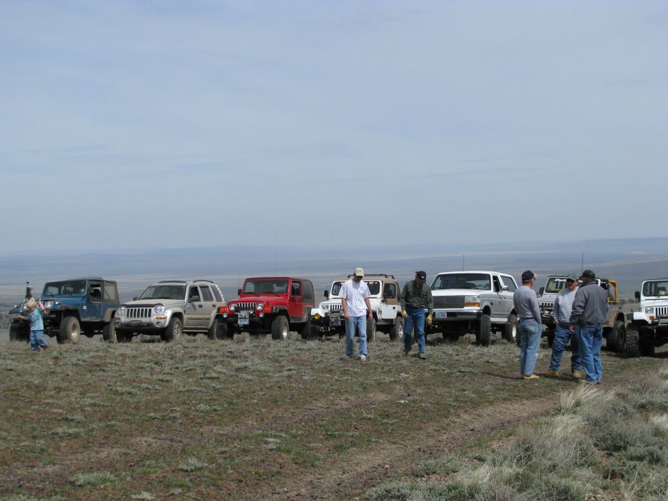 Jeeps and a white Ford Bronco lined up on a sagebrush plateau with drivers talking