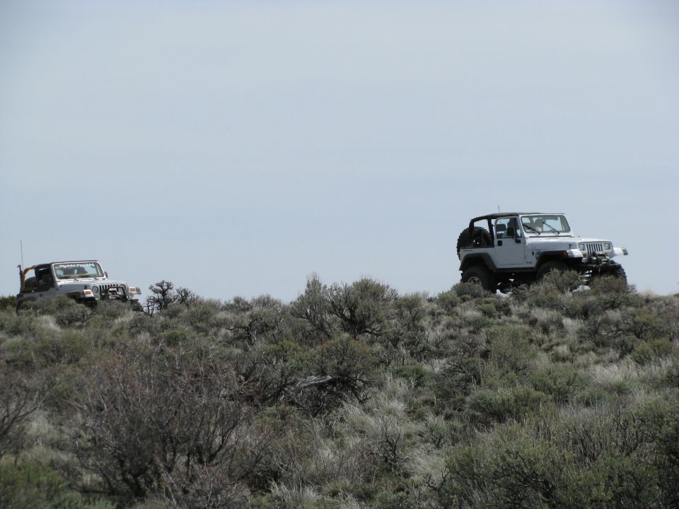 Two white lifted Jeep Wrangler YJs on a sagebrush ridgeline under gray sky