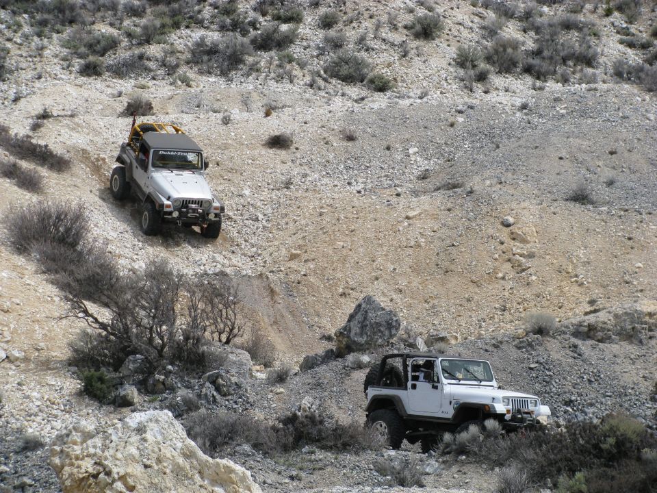 Two lifted white Jeep Wrangler YJs on a chalky desert hillside trail
