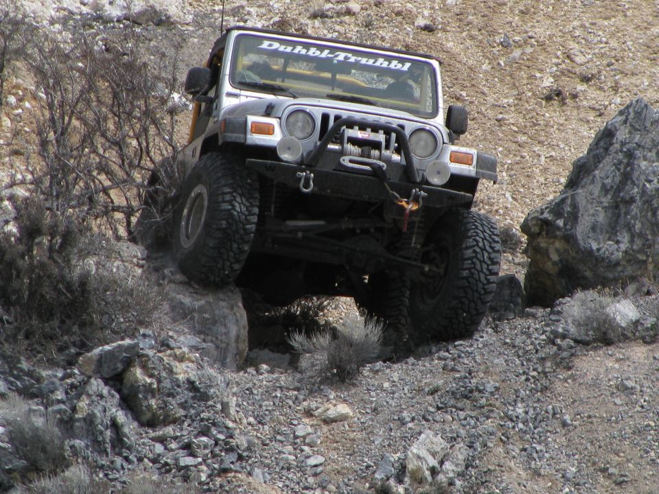 Silver Jeep Wrangler with winch bumper flexing over rocks on a desert trail