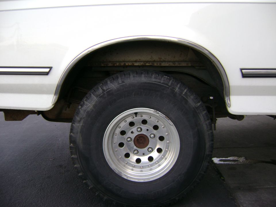 White truck rear wheel with all-terrain tire on polished aluminum wheel and rusty arch