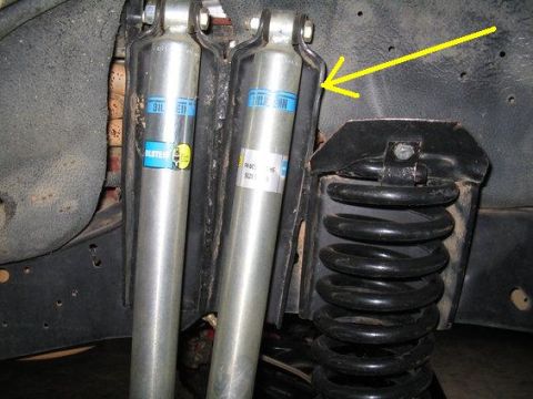 1990 Ford Bronco - A close-up view shows two silver Bilstein shock absorbers mounted near a black coil spring on the underside of a vehicle. A yellow arrow po…