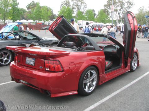 1968 Ford Mustang - A red convertible car with its doors open, parked in a lot with other vehicles.