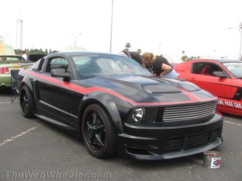 1968 Ford Mustang - A black Ford Mustang with red racing stripes is parked next to a red Mustang at an outdoor car show.