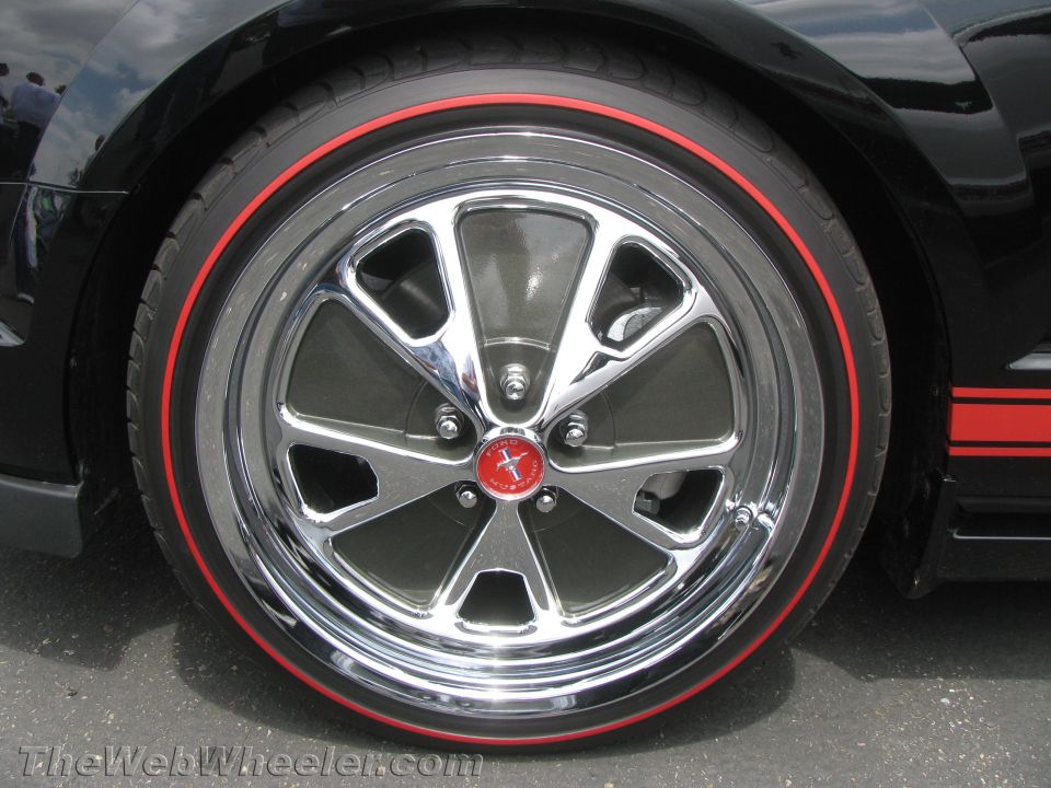 Close-up of a black Ford Mustang wheel with a red stripe on the tire and a red Mustang emblem on the hub