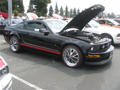 1968 Ford Mustang - A black Ford Mustang with red racing stripes and chrome wheels is parked with its hood open.