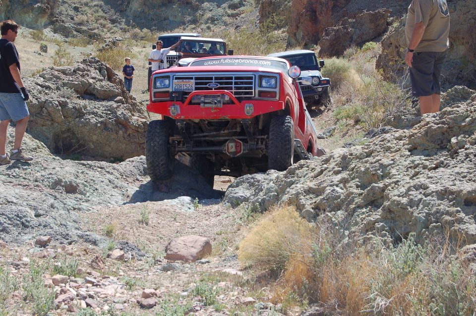 Red 1980s Ford Bronco off-roading on a rocky trail.