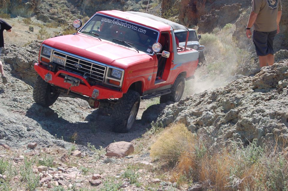 Red 1980s Ford Bronco off-roading on a rocky trail.