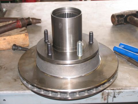 1984 Ford Bronco - A close-up view of a vehicle's brake rotor and hub assembly, with several bolts and a hammer visible on the workbench.