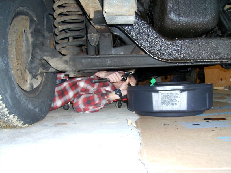 Person working under a vehicle, changing oil.