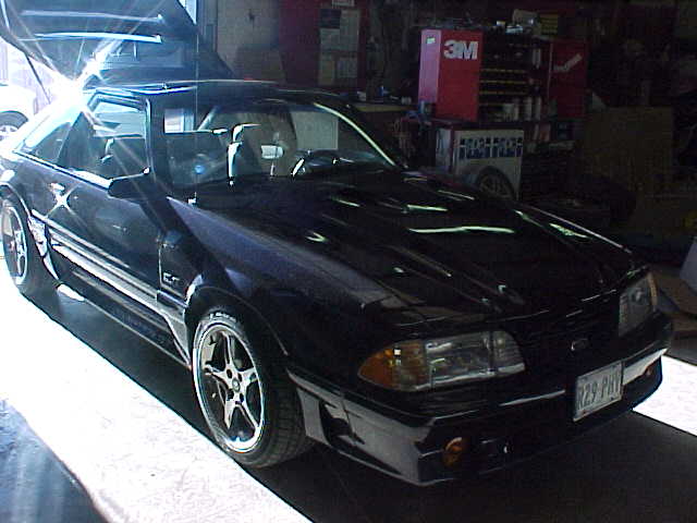 Black Fox-body Ford Mustang hatchback with 5-spoke wheels parked in a garage, front three-quarter view