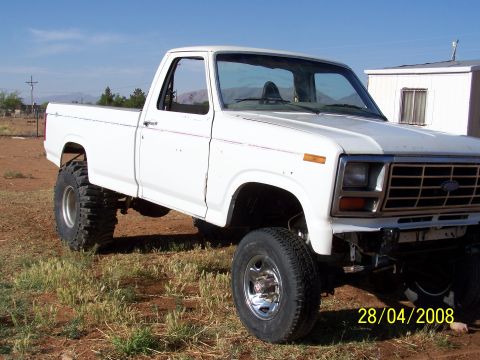 1995 Ford Bronco - A lifted, white, two-door pickup truck with large tires is parked on a dirt lot with sparse vegetation. The truck has a chrome grille and b…