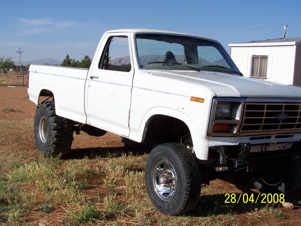 Lifted white pickup truck with large tires, parked on dirt lot.