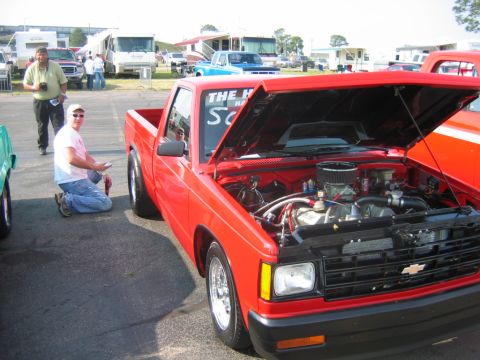 1992 Ford Mustang - A red pickup truck with its hood open, revealing the engine, sits on asphalt with other vehicles in the background.