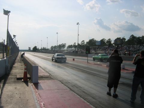 1992 Ford Mustang - A drag race is underway with two cars speeding down the track under a partly cloudy sky.