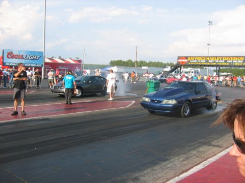 1992 Ford Mustang - A blue 1992 Ford Mustang races down the drag strip, kicking up smoke, with spectators in the background.