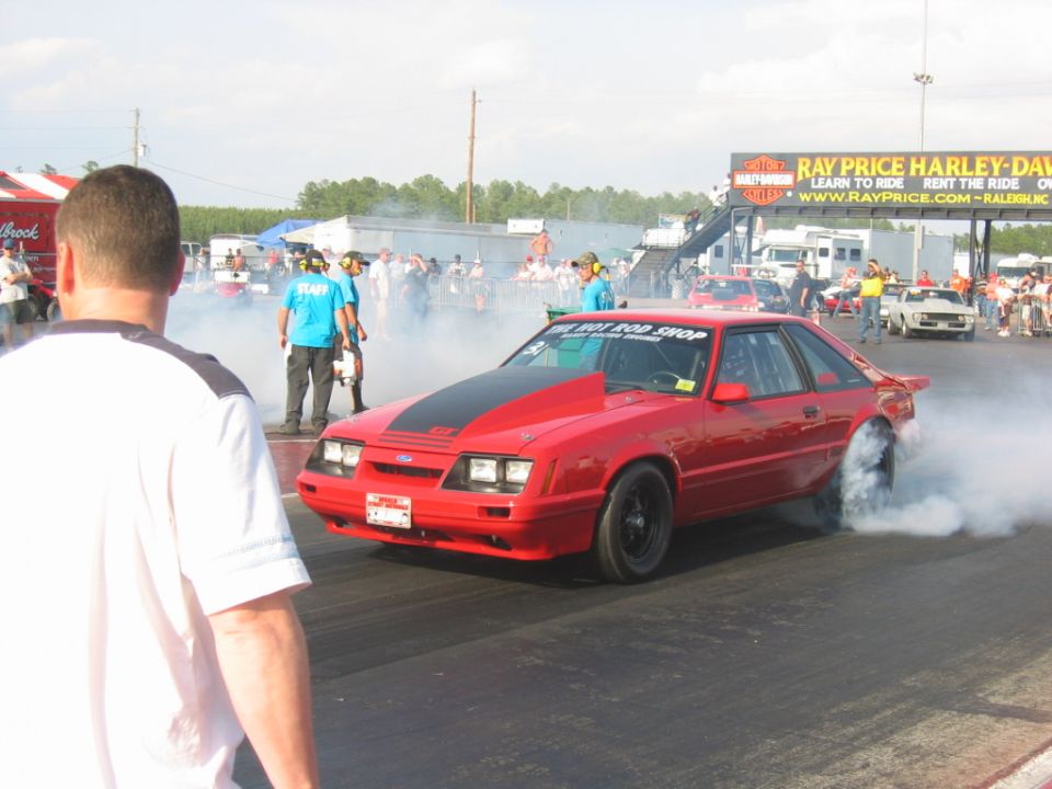 Red drag car with black hood stripe doing a burnout on a drag strip