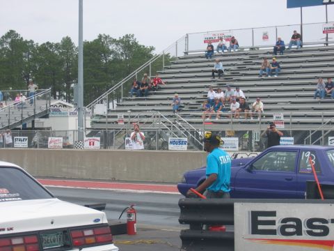 1992 Ford Mustang - A drag race is about to begin with two cars lined up and spectators watching from the stands.