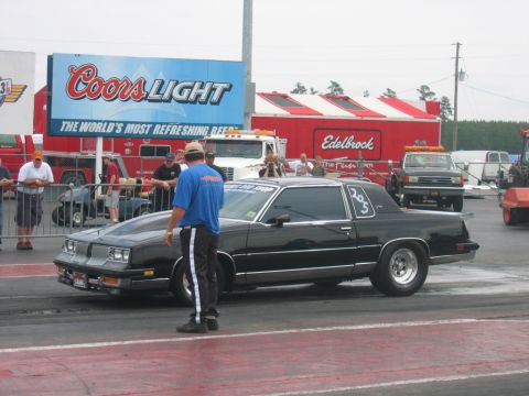 1992 Ford Mustang - A black coupe drag car sits on the track with a crowd watching in the background.