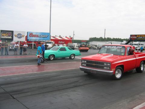 1992 Ford Mustang - Two vehicles on a drag strip, with spectators and advertising in the background.