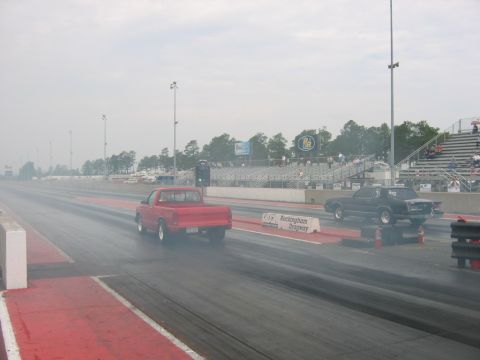 1992 Ford Mustang - Two vehicles compete on a drag strip, with smoke billowing from their tires during the race.