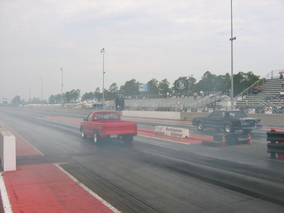 red pickup truck and black car racing on drag strip, smoke coming off tires