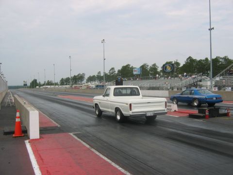 1992 Ford Mustang - Two vehicles line up on a drag strip under an overcast sky, with spectators in the background.