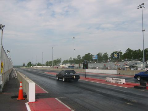 1992 Ford Mustang - A black car races down the drag strip at Rockingham Dragway, with spectators in the stands.