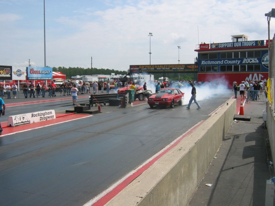 Red sports car with black hood stripe doing a burnout on a drag strip, front view