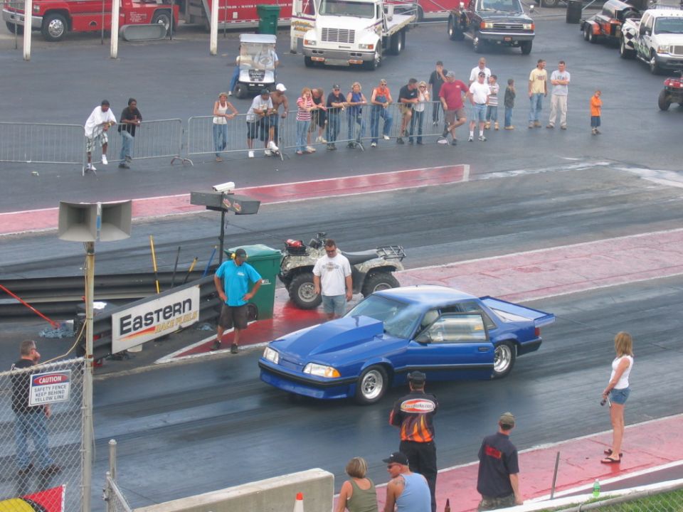 blue drag car with hood scoop on a drag strip, people watching