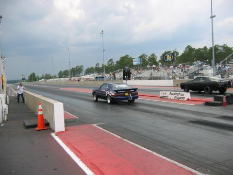 1992 Ford Mustang - Two cars compete in a drag race under a cloudy sky at Rockingham Dragway.