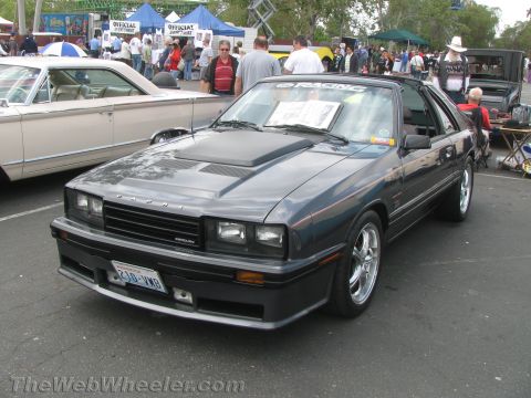 1968 Ford Mustang - A Mercury Capri is parked at an outdoor event, with other vehicles and people in the background.