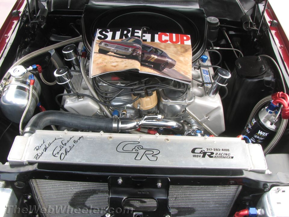 Engine bay with a magazine open on top of the engine. Magazine shows two cars