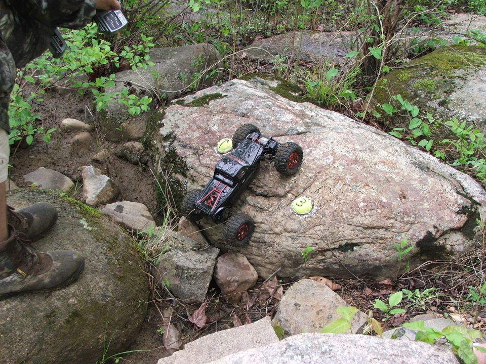 Black remote control rock crawler with red accents on a large rock, marked with yellow circles