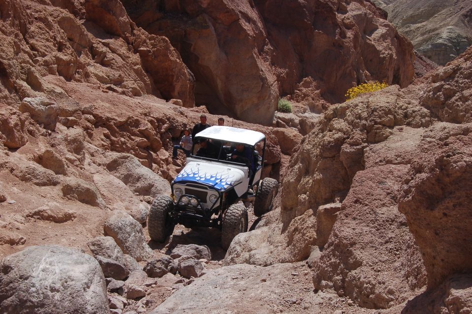 White off-road vehicle with blue flames on hood driving through rocky canyon