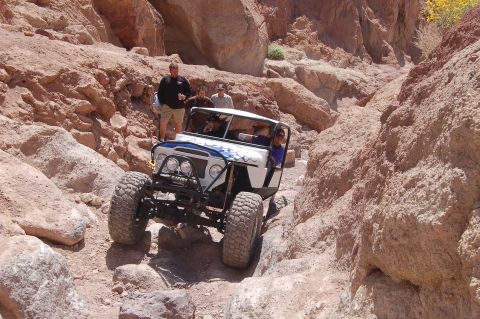 1985 Ford Bronco - An off-road vehicle navigates a narrow, rocky canyon, with several people observing from the side.