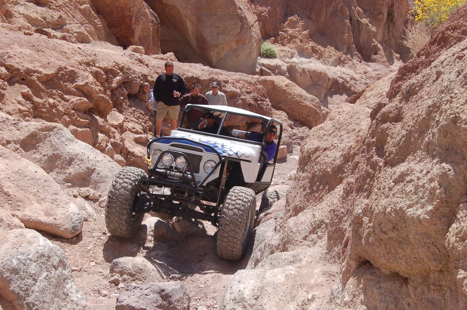 White off-road vehicle with blue graphics driving through a rocky canyon