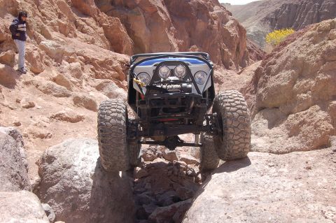 1985 Ford Bronco - Custom off-road vehicle navigates a narrow, rocky passage in a desert canyon.