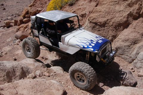 1985 Ford Bronco - This off-road vehicle navigates a rocky, desert terrain with yellow wildflowers in the background.