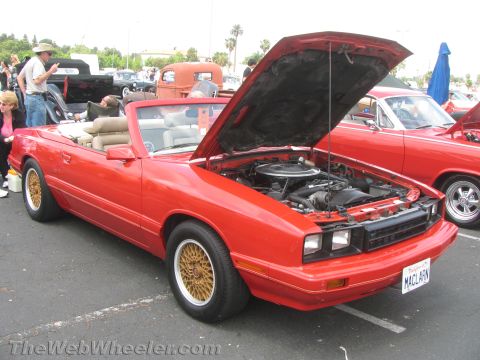 1968 Ford Mustang - This red convertible, likely a Mercury Capri, is displayed with its hood open, revealing the engine bay and gold mesh wheels.