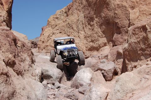 1985 Ford Bronco - Off-road vehicle carefully maneuvers through a challenging rocky canyon trail under a clear blue sky.