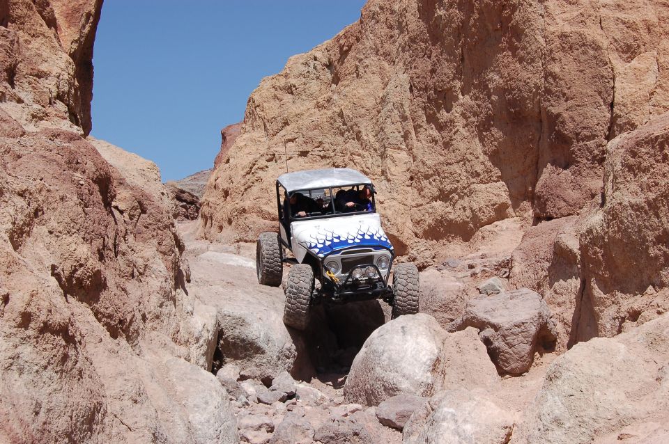 Off-road vehicle with blue flame decals on hood driving through a narrow, rocky canyon with red rock formations